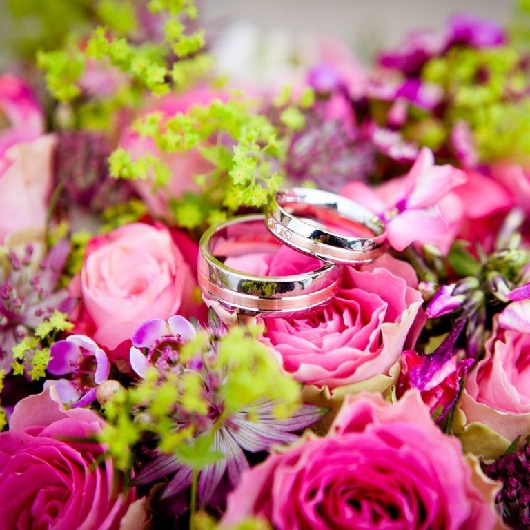 Anillos de boda entre flores rosadas y verdes.